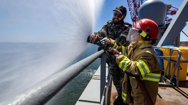 Royal Australian Navy Leading Seaman Marine Technician Hayden Brown demonstrates fire fighting techniques to a member of the public during the HMAS Choules open day