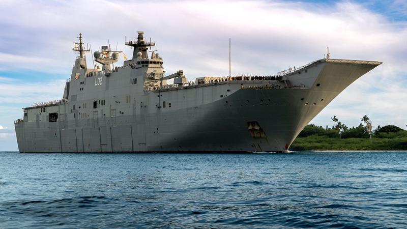 HMAS Canberra pulling into a low lying tropical coast.