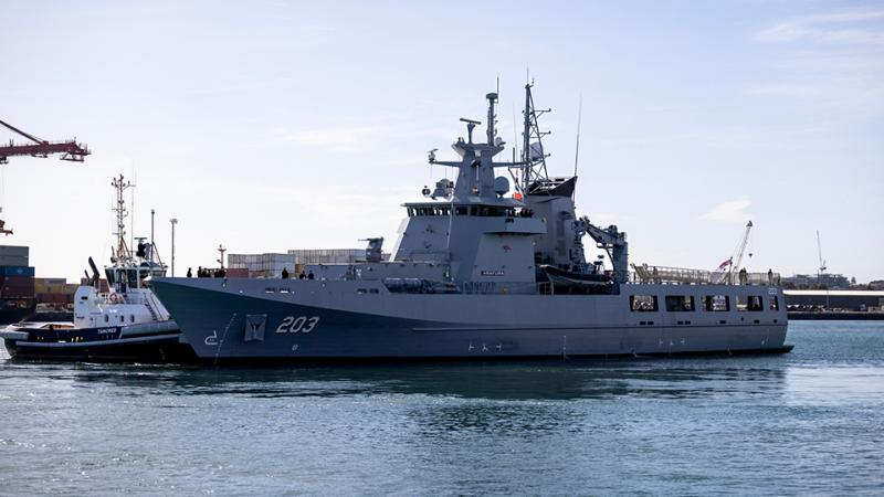 A large vessel in the water in front of a shipping terminal.