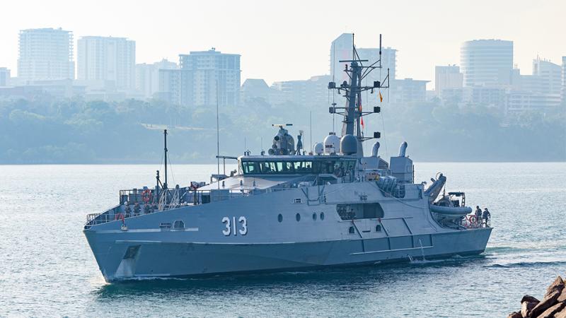 A large grey ship with the number 313 in a harbour with city buildings in the background.